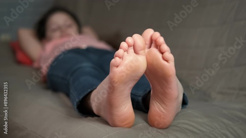 Teen with bare feet on sofa. A view of young girl with bare feet resting on the sofa with bare feet. A concept of leisure time during childhood.