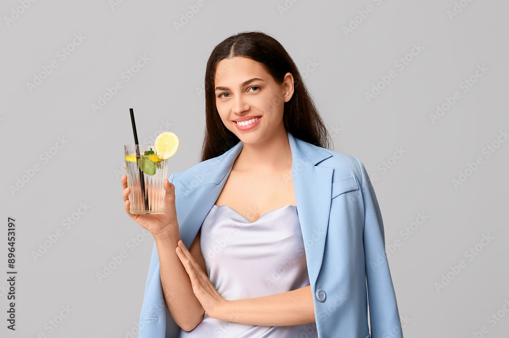 Beautiful young happy woman with glass of fresh lemonade on grey background Beautiful young happy woman with glass of fresh lemonade on grey background