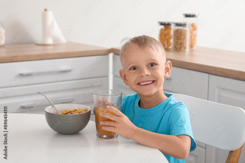 Happy little boy eating cornflakes with milk and drinking juice on breakfast at home