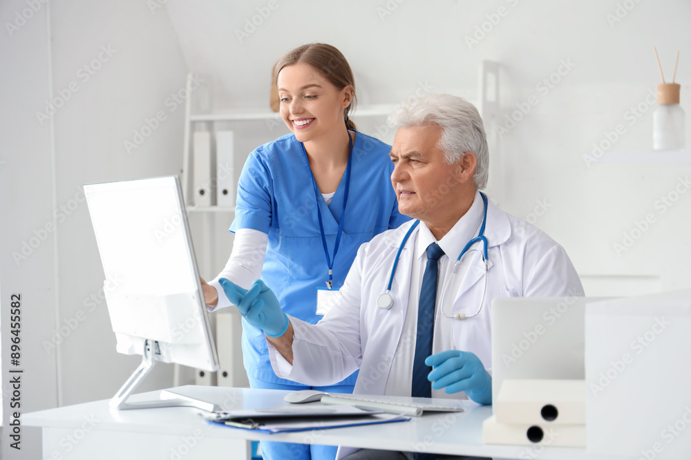 Mature doctor and nurse working with computer at table in clinic Mature doctor and nurse working with computer at table in clinic