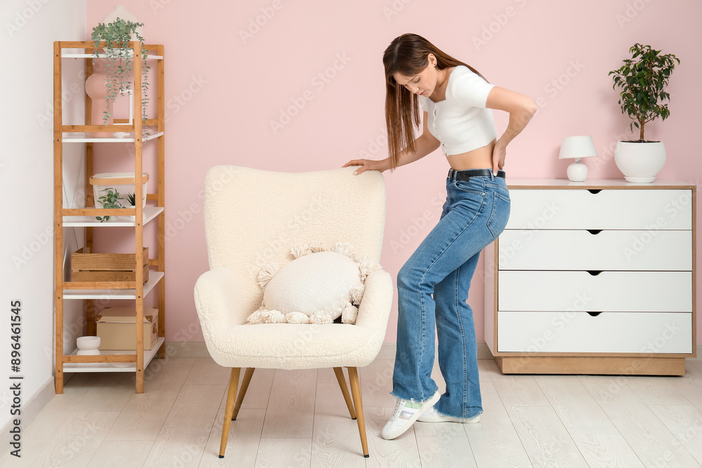 Young woman suffering from back pain in room Young woman suffering from back pain in room