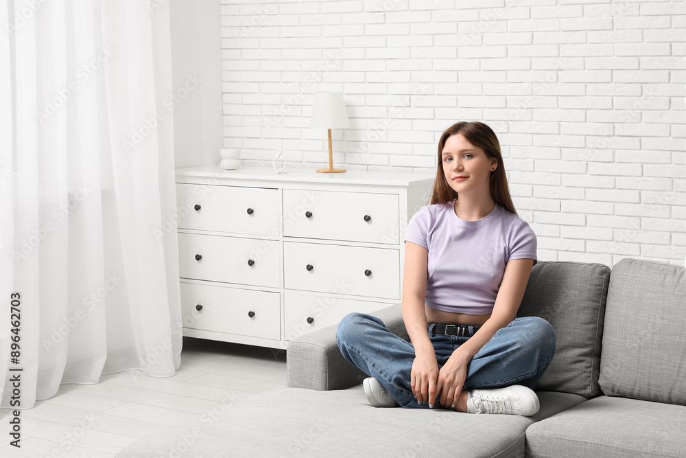 Pretty young woman sitting on comfortable sofa in living room