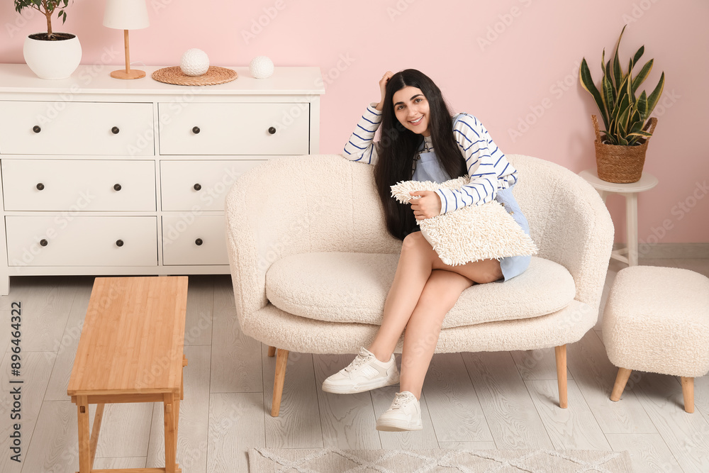 Pretty young woman with pillow sitting on white sofa in stylish living room