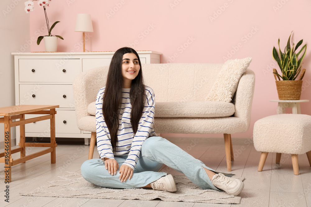 Pretty young woman sitting on floor near sofa in stylish living room Pretty young woman sitting on floor near sofa in stylish living room