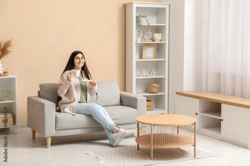 Pretty young woman with cup sitting on grey armchair in stylish living room Pretty young woman with cup sitting on grey armchair in stylish living room