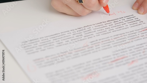 Professional school or college teacher grades a homework exam papers of students. Woman checks essay, crosses wrong words, corrects it with red pen.