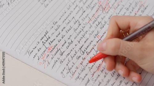 Professional school or college teacher grades a homework exam papers of students. Woman checks essay, crosses wrong words, corrects it with red pen.