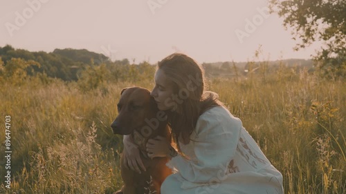 young cheerful woman playing with her dog outdoors in beautiful countryside field. Female and ridgeback dog walking and having fun