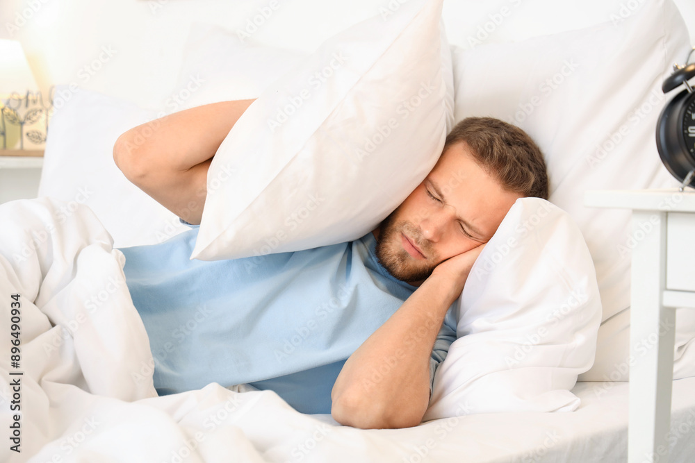 Stressed young man on bed with pillow suffering from insomnia at home