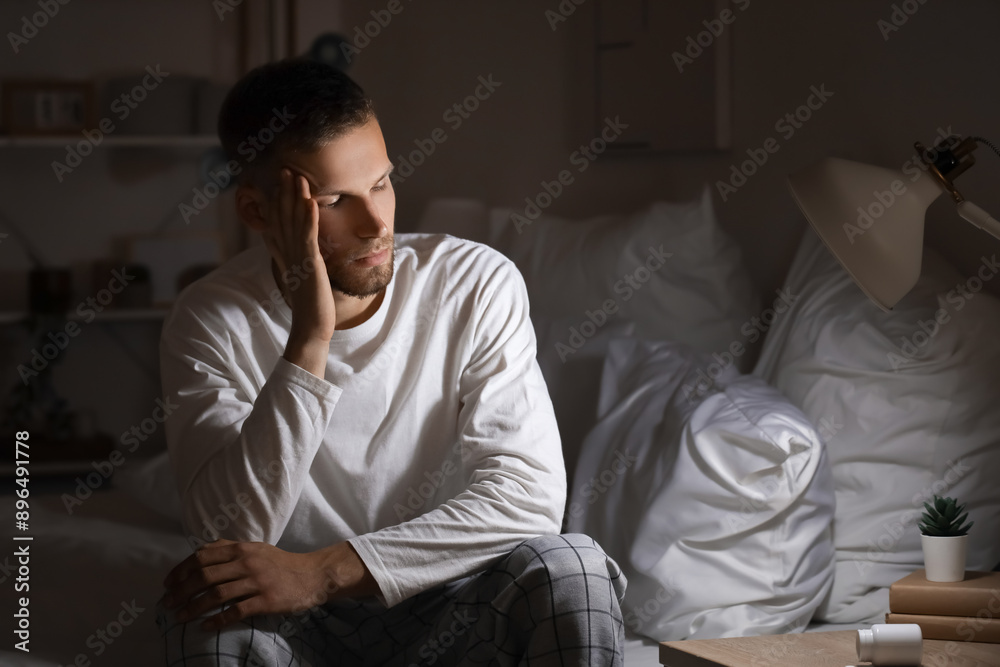Young man suffering from insomnia and sitting on bed in bedroom at late night
