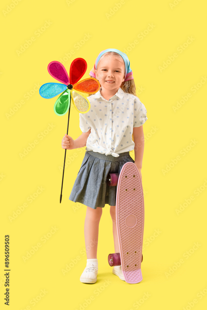 Cute little girl with toy windmill and skateboard on yellow background Cute little girl with toy windmill and skateboard on yellow background