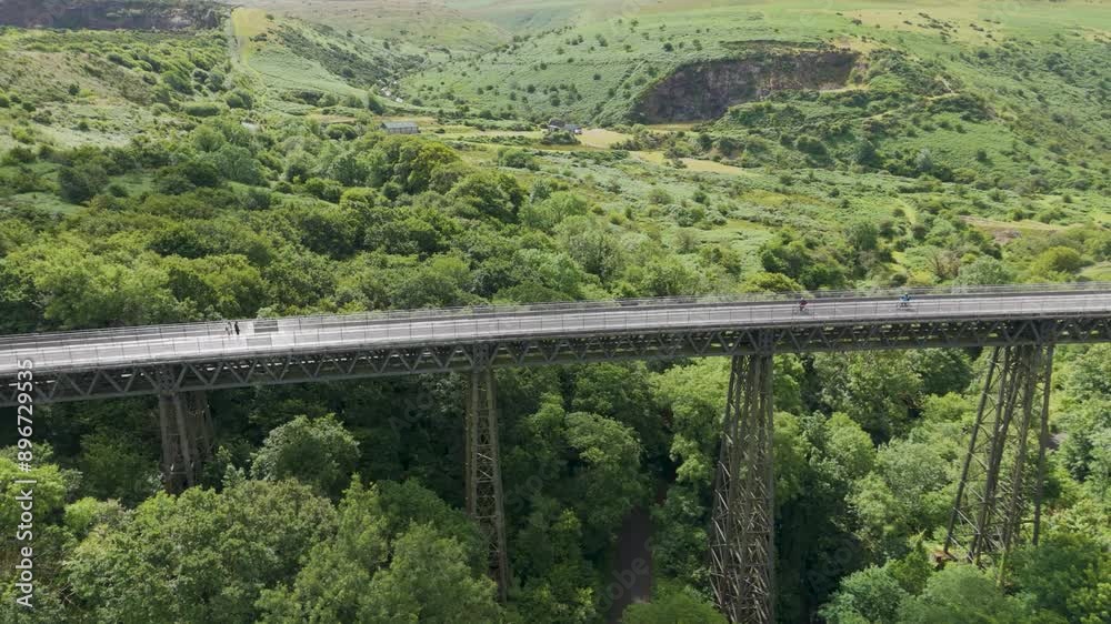 Two cyclists crossing an old viaduct with a scenic backdrop of lush green hills and valleys Two cyclists crossing an old viaduct with a scenic backdrop of lush green hills and valleys