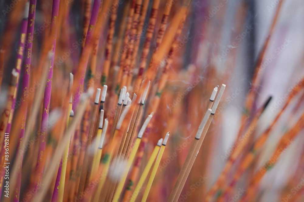 A close up of bunch of lit incense sticks with burning ash in blurred background inside Buddhist temple in the concept of beliefs and Buddhism religion. A close up of bunch of lit incense sticks with burning ash in blurred background inside Buddhist temple in the concept of beliefs and Buddhism religion.