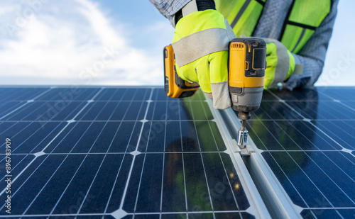 close up on hands of an unrecognizable engineer installing and giving maintenance to solar panels using a drill, professional technician working on a roof with blue sky background