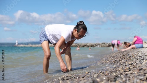 Asian woman bending over searching for Petoskey stones in Petoskey Michigan. photo