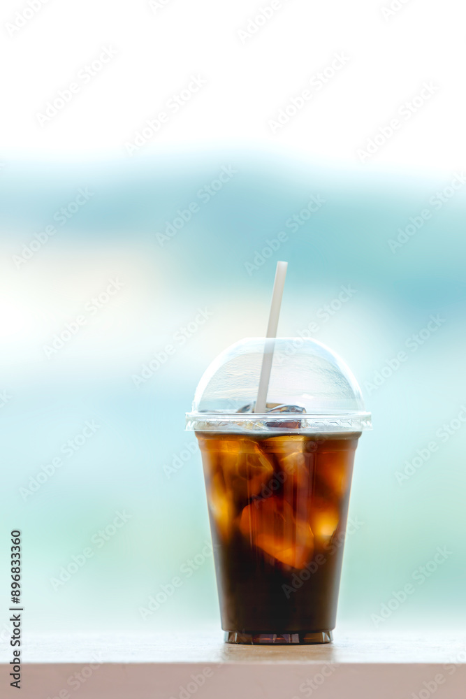 Iced Americano in a take-out plastic cup. Window with a panoramic view