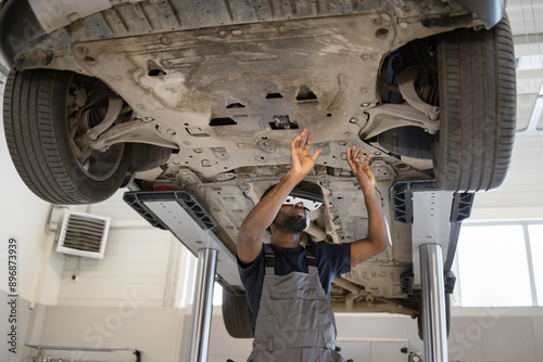 Mechanic using 3D technology inspects vehicle underside for potential malfunctions. Modern automotive garage. Maintenance, repair, and diagnostics concept. High-tech equipment.