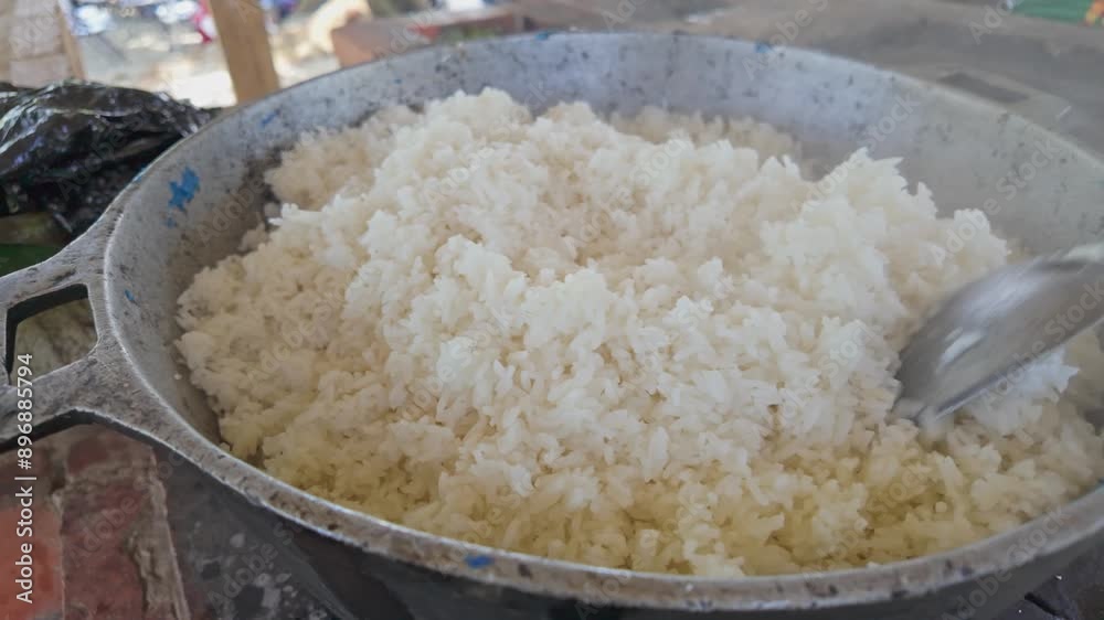 Rice cooked with firewood in an iron container, stirred with a large spoon, emitting steam on a sunny day in the field. Traditional rice preparation in a rustic and natural environment Rice cooked with firewood in an iron container, stirred with a large spoon, emitting steam on a sunny day in the field. Traditional rice preparation in a rustic and natural environment