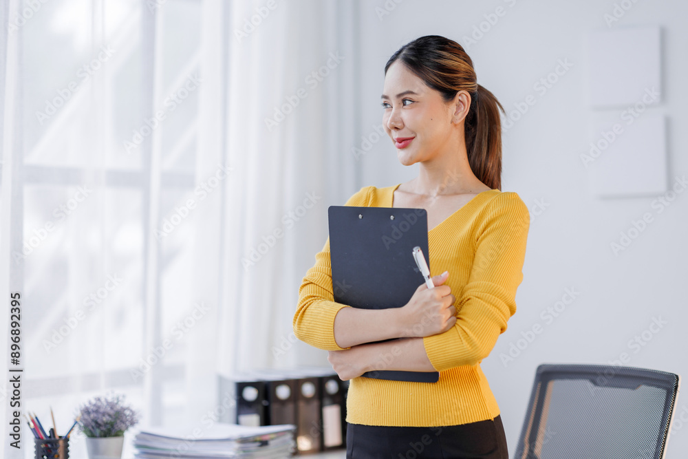 Portrait of a happy asian woman crossed arms hold with clipboard in the workplace office. Portrait of a happy asian woman crossed arms hold with clipboard in the workplace office.