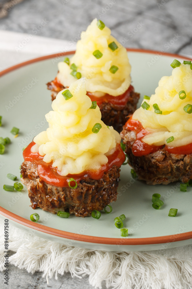 Delectable little Meatloaf Muffins with mashed potatoes on top closeup on the plate on the table. Vertical