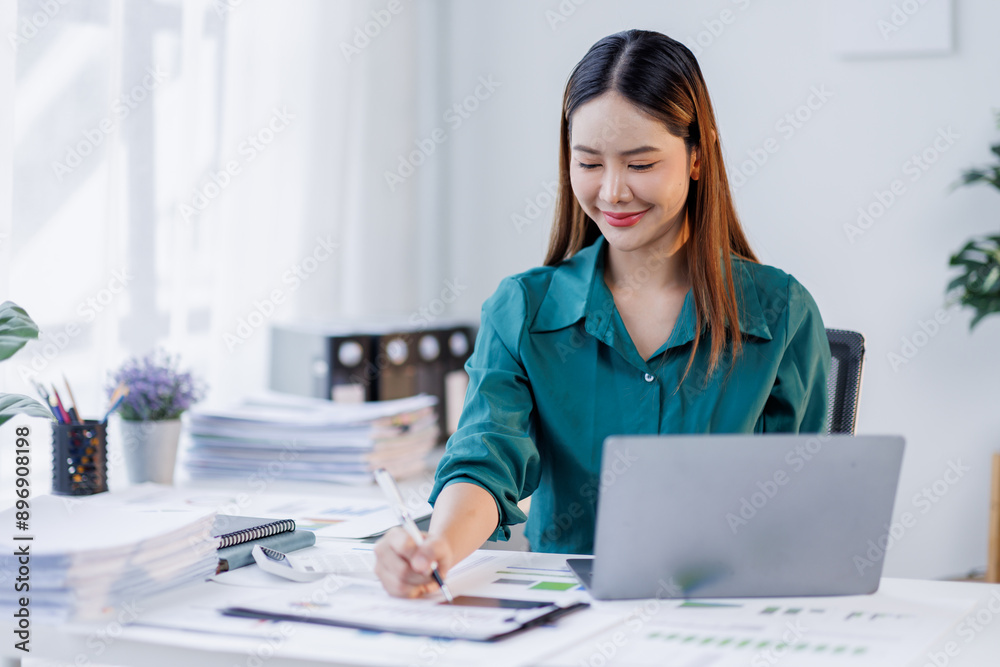 Asian woman in the workplace Work Hard writing notes on a pad from her laptop computer with analytical charts and graphs in front of her, business people concept Asian woman in the workplace Work Hard writing notes on a pad from her laptop computer with analytical charts and graphs in front of her, business people concept