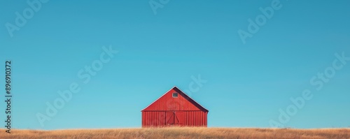 Red barn on a grassy hill with clear blue sky, minimalistic rural scene photo