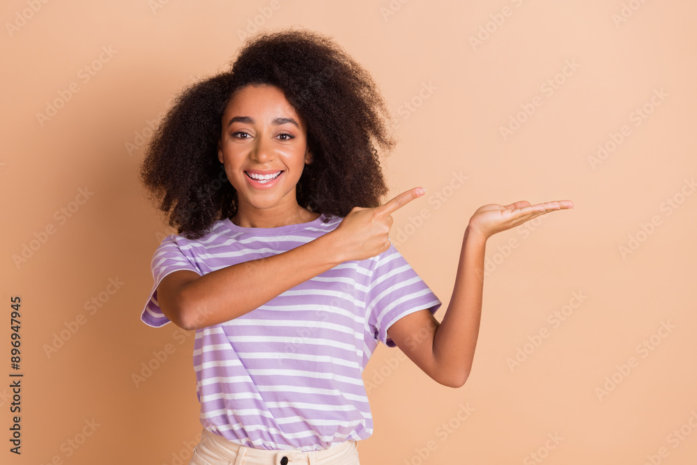 Photo of nice young woman direct finger hold empty space wear striped t-shirt isolated on beige color background Photo of nice young woman direct finger hold empty space wear striped t-shirt isolated on beige color background