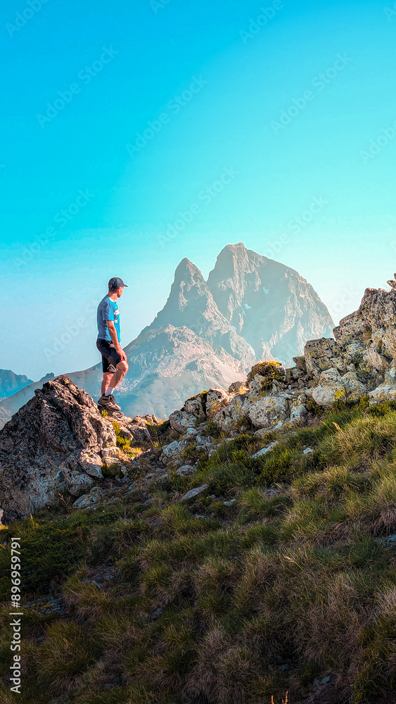 Obraz premium Impressive view from the ascent to Espelunciecha Peak in the Pyrenees, with a young man enjoying the Ibón de Anayet, Anayet Peak and the imposing Midi d'Ossau in the background. 
