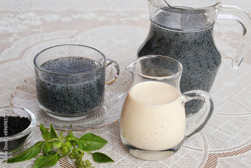 A jar of fresh milk is placed in front. Fully swollen basil seeds in a glass with a big pitcher Black seeds and fresh shoots All placed in a set On a white plastic tablecloth

