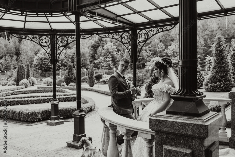 Obraz premium A bride and groom are standing in front of a gazebo, with the bride wearing a white dress