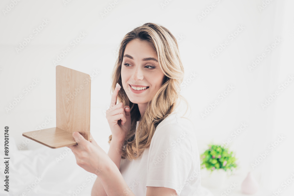 Photo of positive girl applying cream clean face look mirror in day light room Photo of positive girl applying cream clean face look mirror in day light room