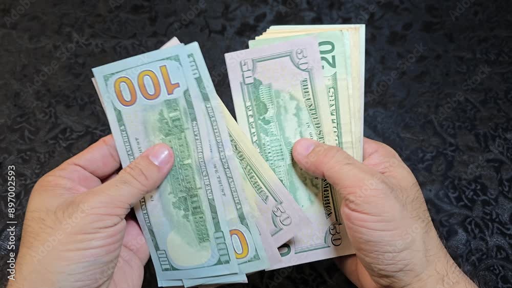 Close-up of hands counting US banknotes on a table with a dark background. Close-up of hands counting US banknotes on a table with a dark background.