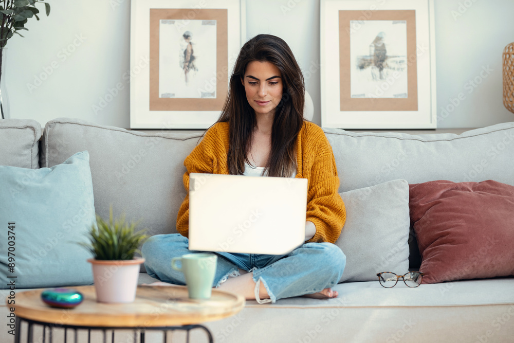 Beautiful young woman working with her laptop while sitting on a couch at home. Beautiful young woman working with her laptop while sitting on a couch at home.