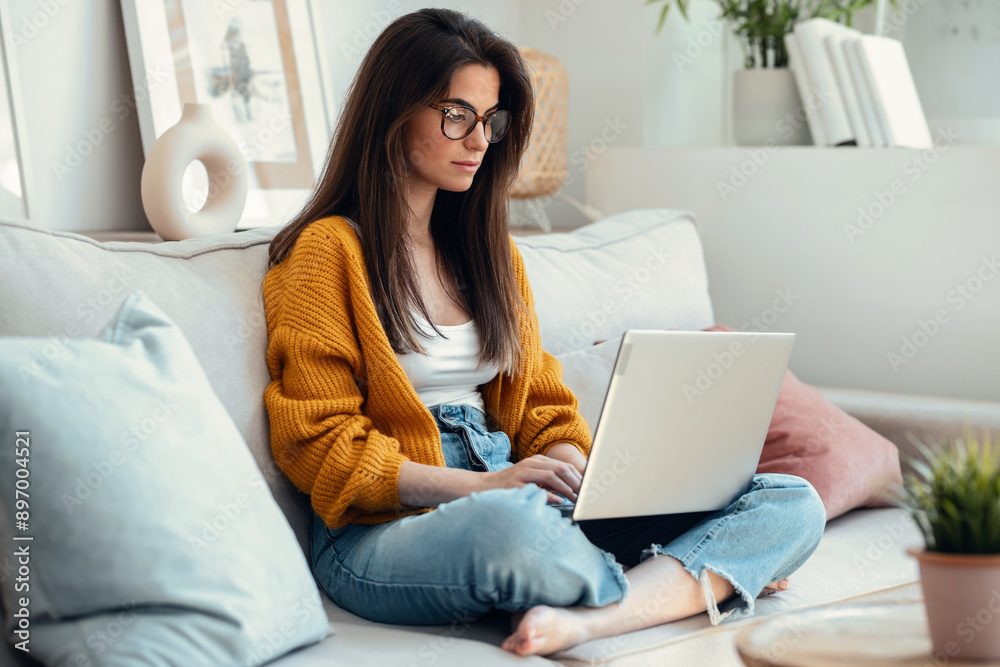 Beautiful young woman working with her laptop while sitting on a couch at home. Beautiful young woman working with her laptop while sitting on a couch at home.
