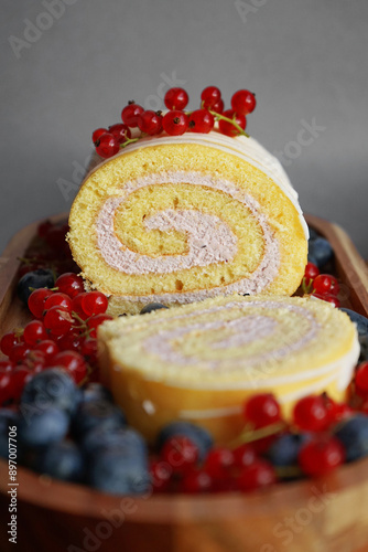 Sponge roll with cream and fresh blueberries and red currants on a wooden tray on a gray background