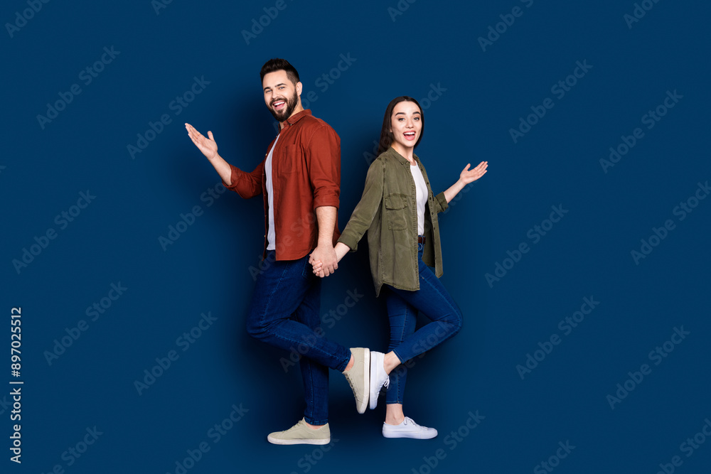 Photo of cheerful glad couple wife husband wear stylish clothes hold hands announce discount isolated on dark blue color background Photo of cheerful glad couple wife husband wear stylish clothes hold hands announce discount isolated on dark blue color background