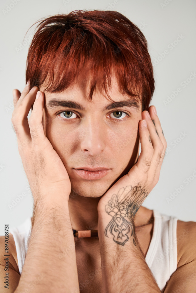 A stylish young man with red hair holds his hands to his face, deep in thought, against a grey background. A stylish young man with red hair holds his hands to his face, deep in thought, against a grey background.