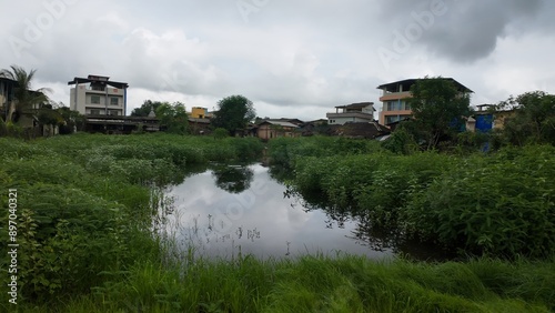 Tranquil water body amidst a lush green meadow, with a cloudy sky overhead, capturing the essence of the monsoon season.