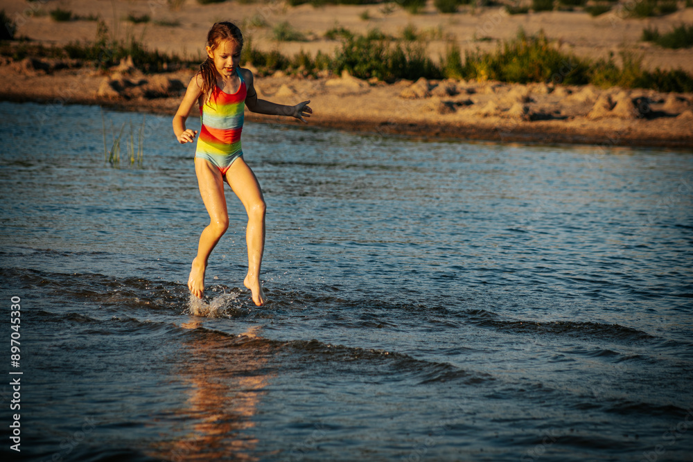 Naklejka premium A girl in a colorful swimsuit walking through the ocean waves, enjoying the summer day. The image captures a serene and playful moment by the sea