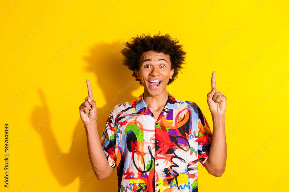 Photo of nice young man point fingers up empty space wear shirt isolated on bright yellow color background Photo of nice young man point fingers up empty space wear shirt isolated on bright yellow color background