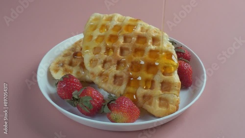 pouring honey over croffles or waffles and strawberries in white plate isolated pink background