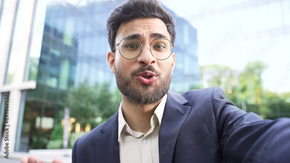 POV Smiling businessman in formal suit talking on a video call using mobile phone standing on street near an business office building. Happy man worker greeting, communicating online looking at camera POV Smiling businessman in formal suit talking on a video call using mobile phone standing on street near an business office building. Happy man worker greeting, communicating online looking at camera