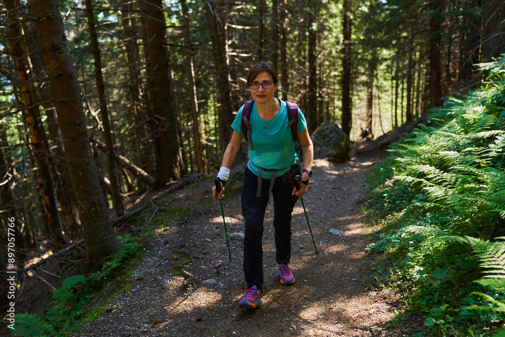 Fototapeta premium Woman hiker with backpack and poles on a trail