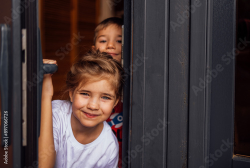 Close-up of cute children peeking out of the doorway. Little brother and sister open the front door. Cute kids meet their parents or guests.