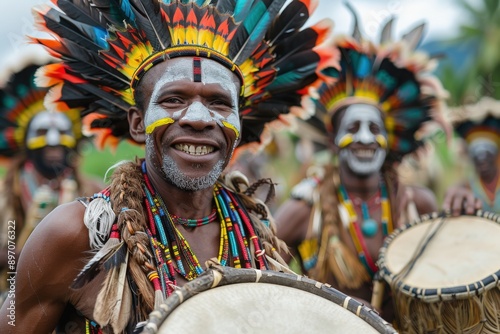 A tribal man, showcasing vibrant face paint and dressed in an elaborate headdress, smiles engagingly while participating in a traditional event with fellow tribesmen outdoors. photo