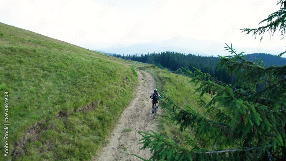 Cyclist man riding electric mountain bike outdoors. Aerial view of male tourist biking along grassy trail in the mountains, wearing helmet and backpack. Concept of sport, active leisure and nature. Cyclist man riding electric mountain bike outdoors. Aerial view of male tourist biking along grassy trail in the mountains, wearing helmet and backpack. Concept of sport, active leisure and nature.