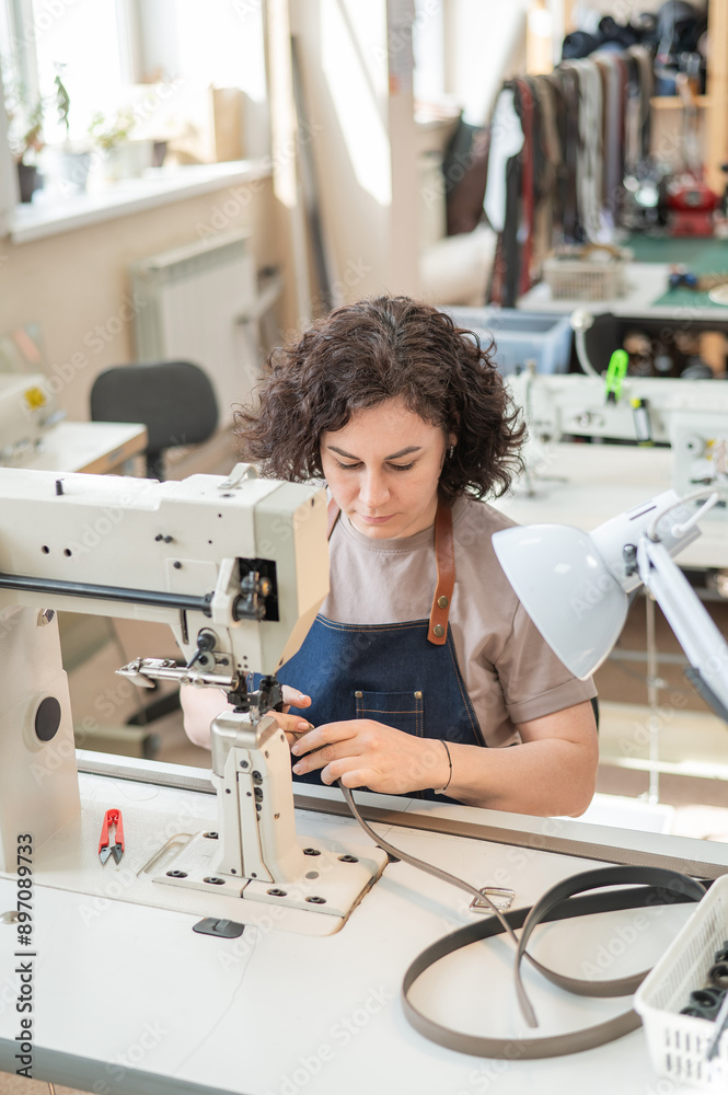 A woman tanner sews a leather belt on a sewing machine. Vertical photo. A woman tanner sews a leather belt on a sewing machine. Vertical photo.