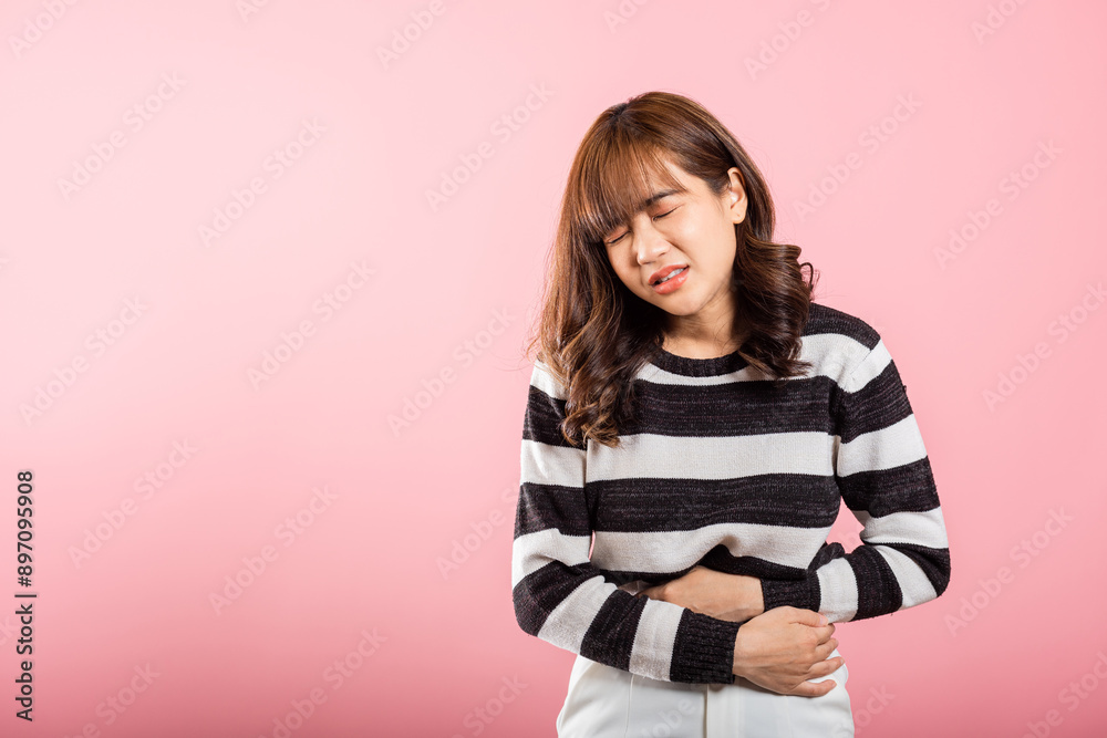 Portrait of Asian beautiful young woman has stomachache, female abdominal pain suffering from stomach ache, studio shot isolated on pink background, period pain, Health and medical gastritis concept