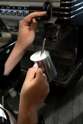 An unrecognizable girl prepares milk froth in a coffee machine. Shooting from the back. The process of whipping milk foam for cappuccino. Vertical photo