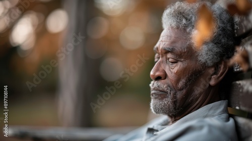 An elderly person with grey hair is resting on a wooden bench in an autumn park, surrounded by colorful leaves, embodying peace and reflection.